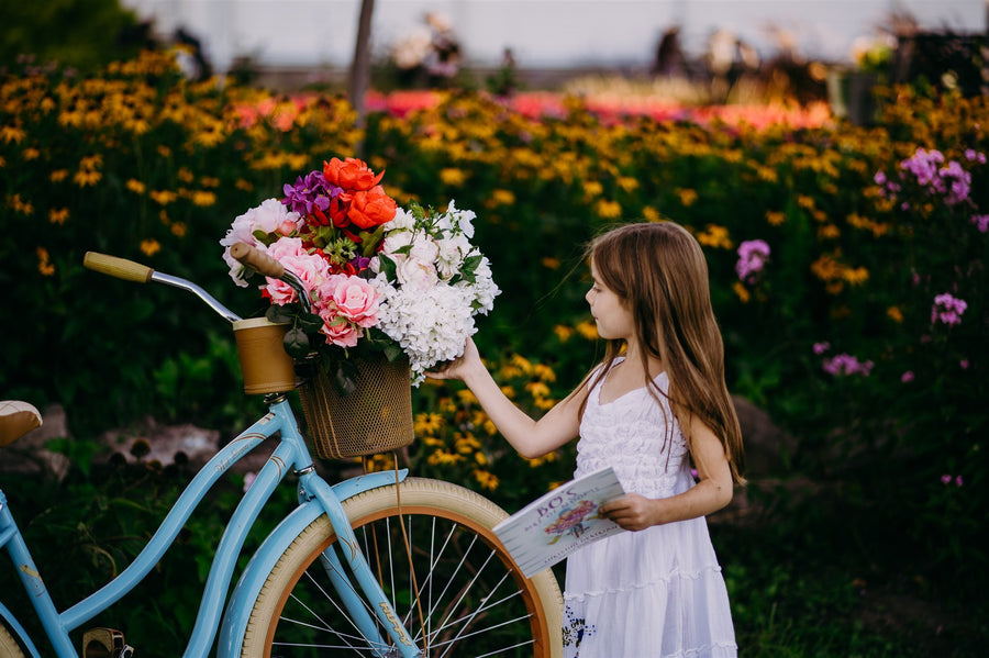 Girl in a white dress reaching for the flowers in a bicycle basket