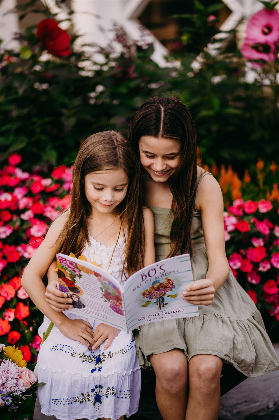 Two sisters reading Bo's Bike of Blooms among pink flowers