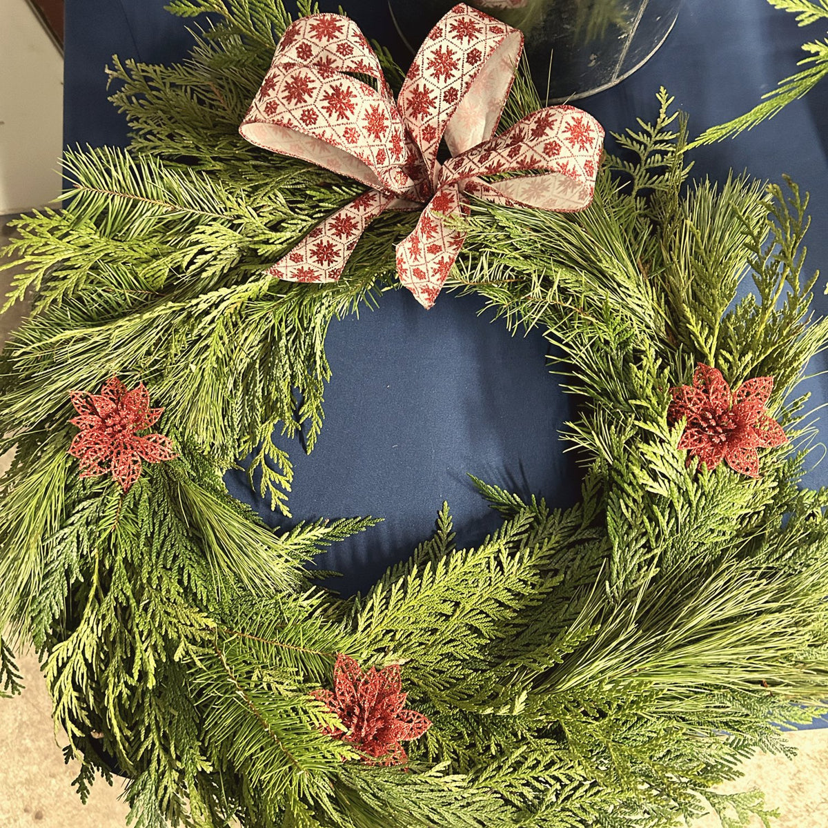 Couronne de cèdre avec un nœud rouge et blanc et des accents de poinsettias rouges