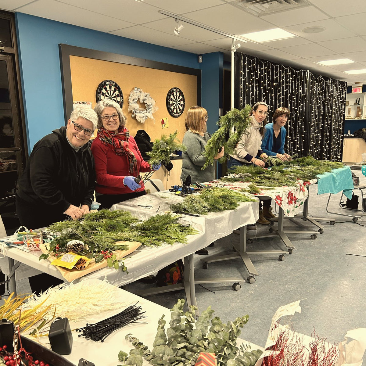 Participantes confectionnant leurs couronnes autour d'une table garnie de verdure fraîche