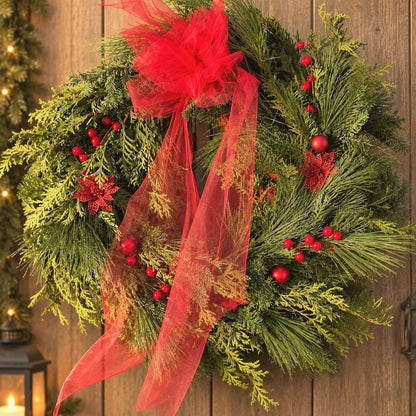 Couronne de Noël en verdure fraîche avec un nœud de tulle rouge et des baies rouges sur une porte en bois