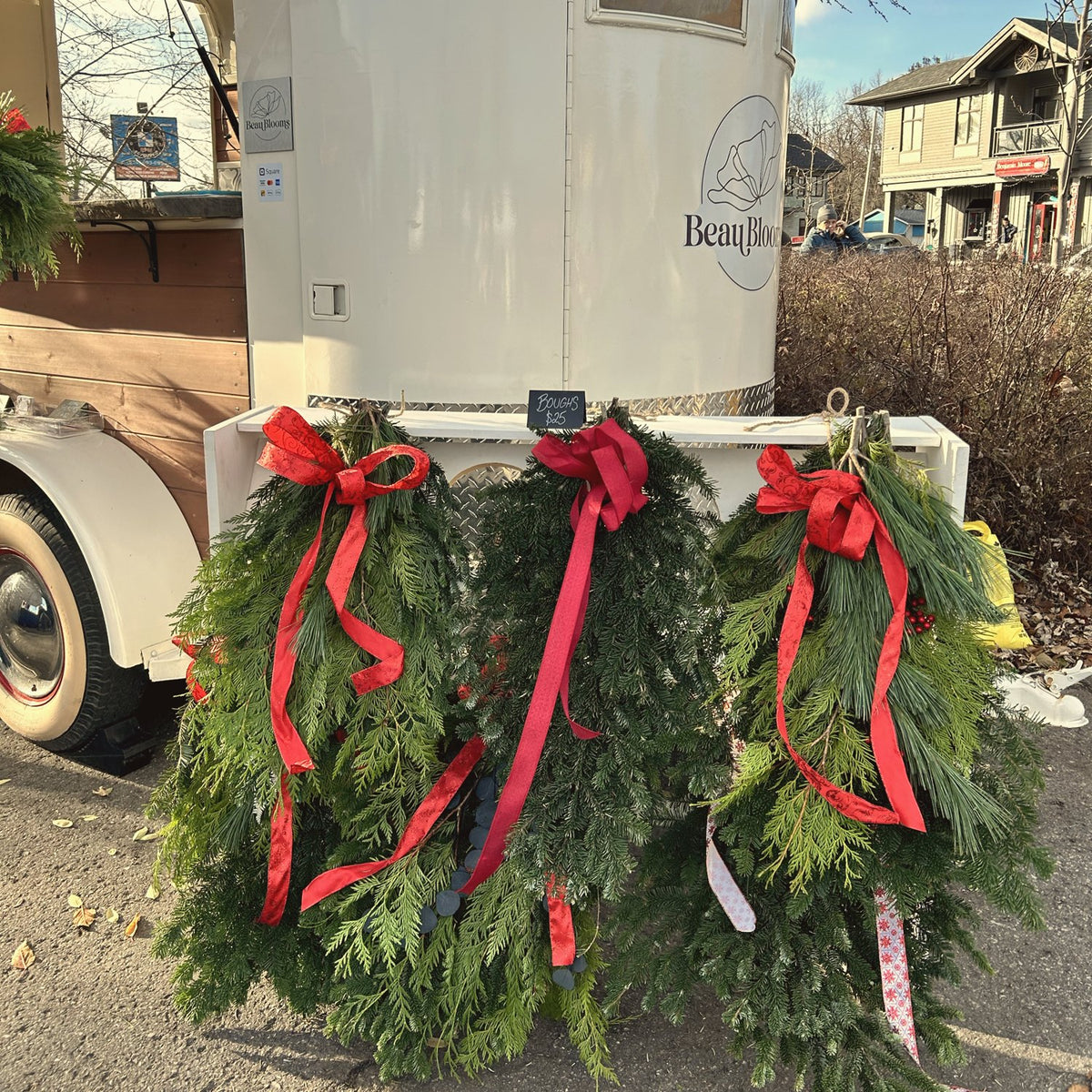 Trois couronnes fraîches à rubans rouges devant la remorque vintage de Beau Blooms